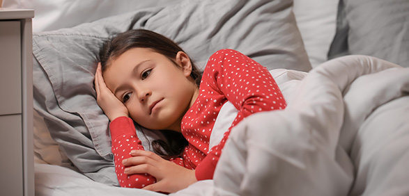 a girl in red pajamas laying awake in a bed