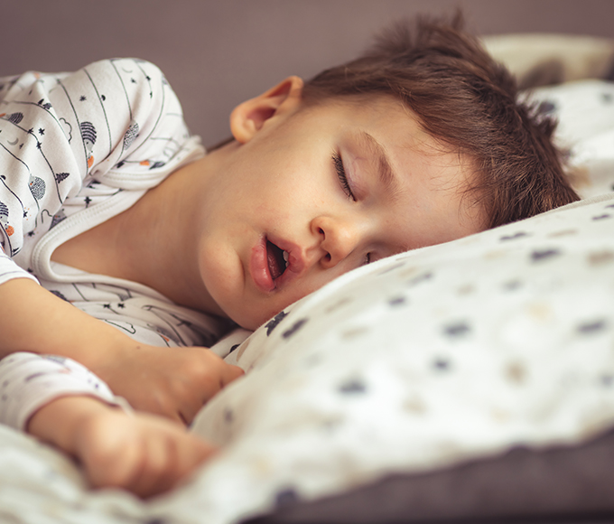 a young boy wearing patterned pajamas sleeping on a polka-dot bed