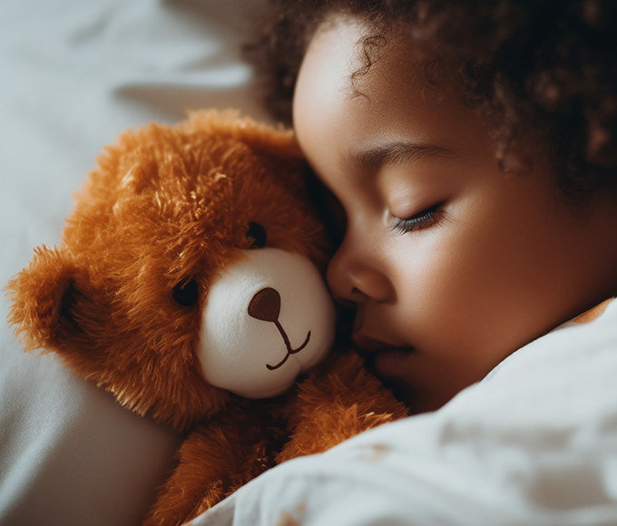 a young boy sleeping with a teddy bear in bed